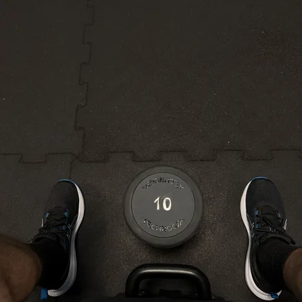 A dumbbell on the gym floor between a pair of training shoes