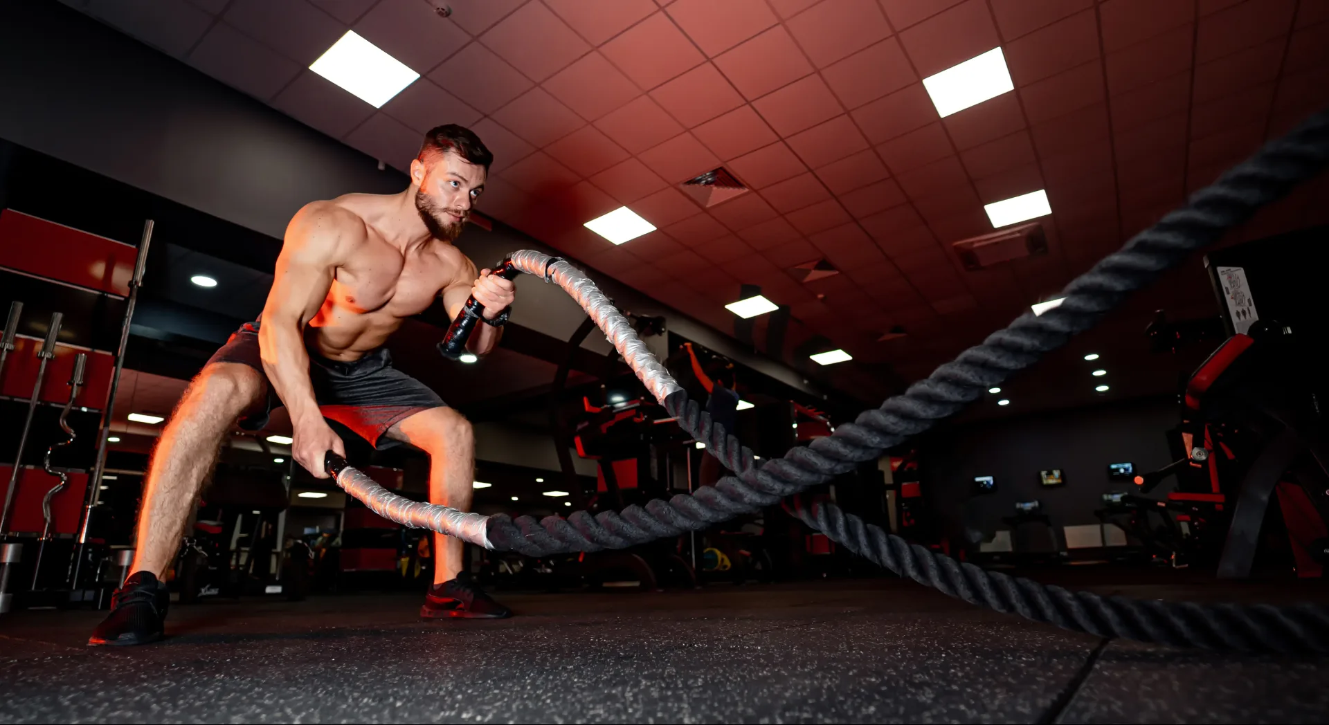An athlete swinging battle ropes in a red-lit gym