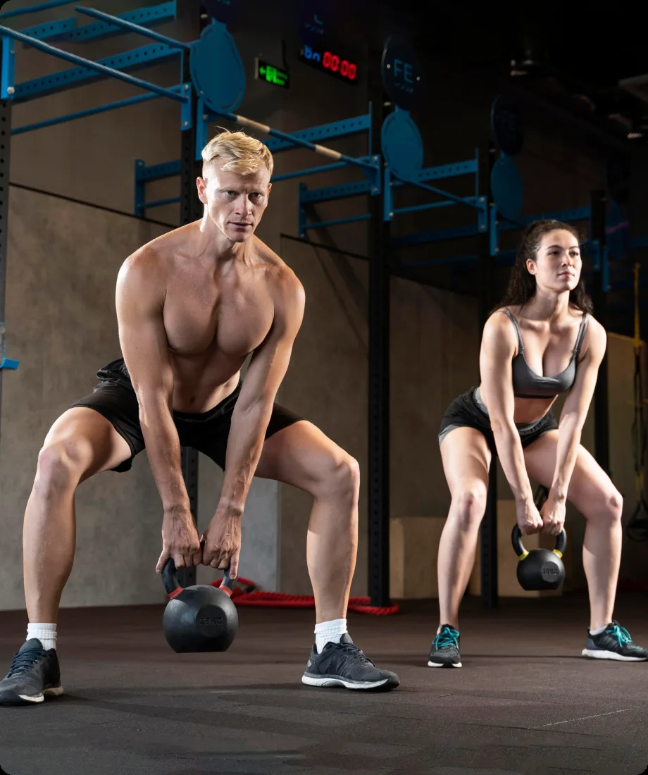 Two FORGE trainers demonstrating a kettlebell squat side by side