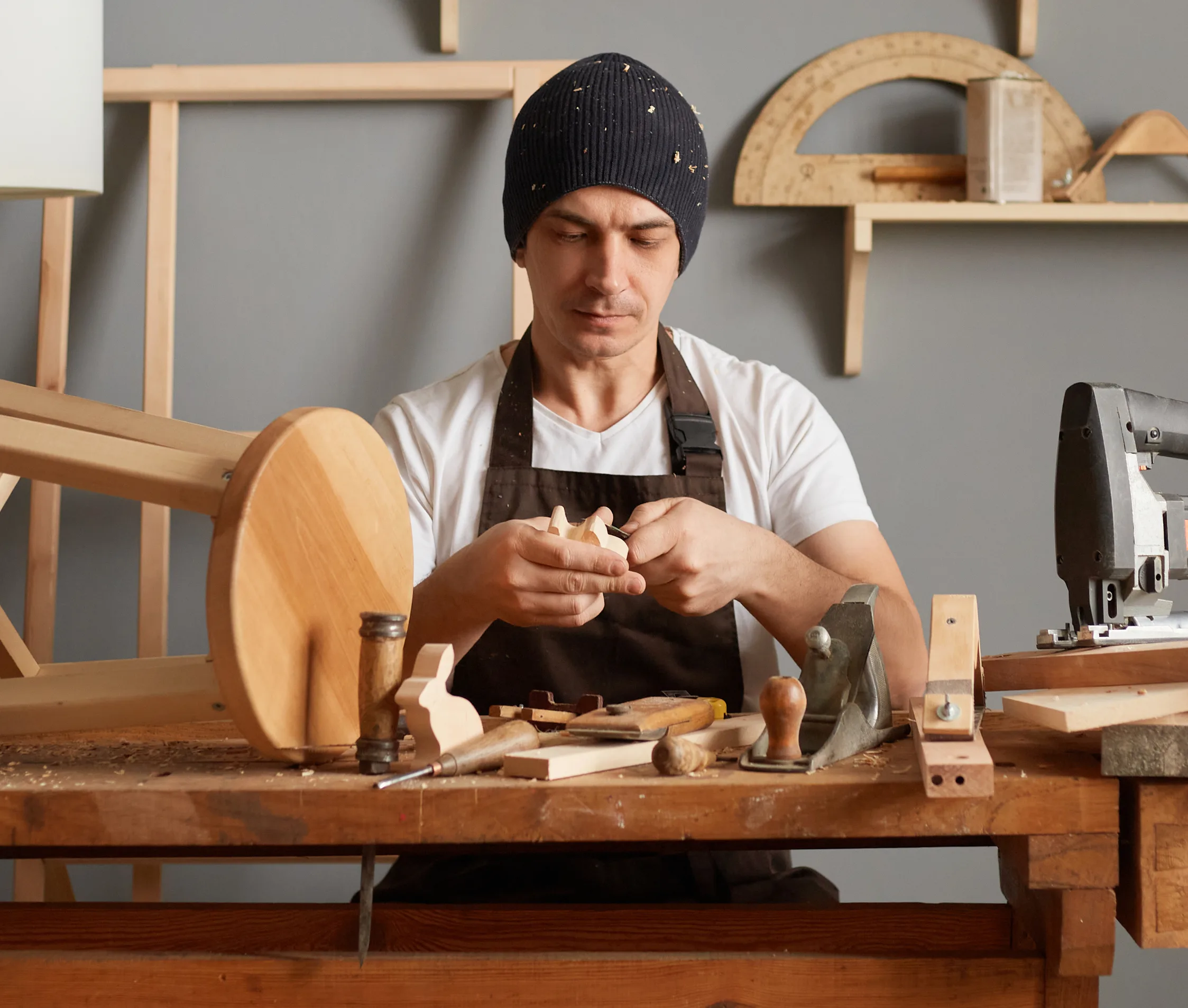 Woodworker shaping a stool top at a bench of hand tools