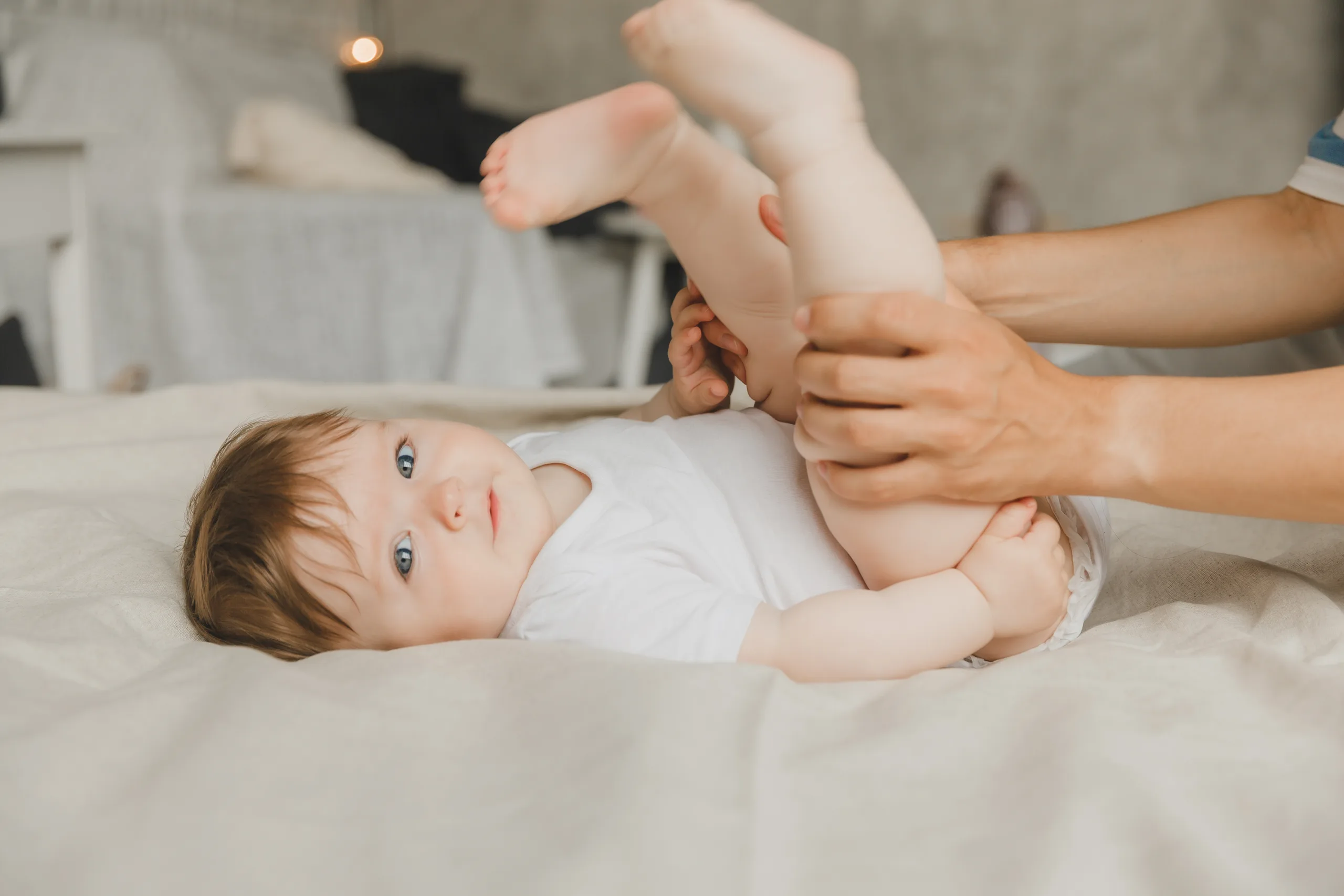 Parent gently holding a baby’s legs while changing them on a white bed
