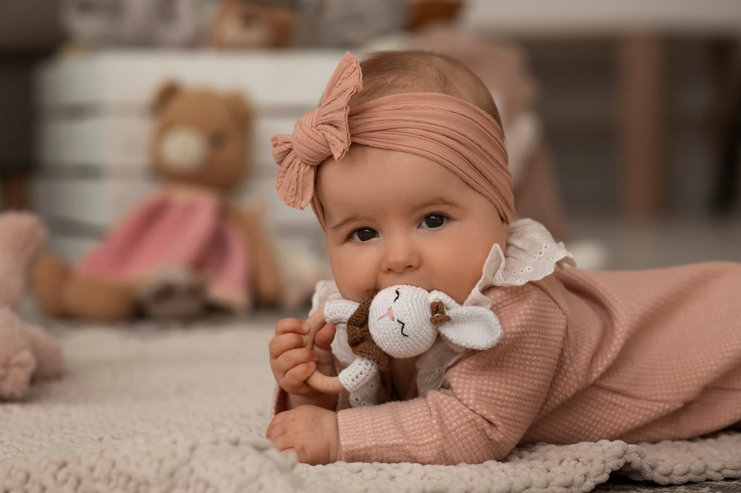 Baby in a pink knit outfit lying on a soft blanket with a crochet lamb rattle