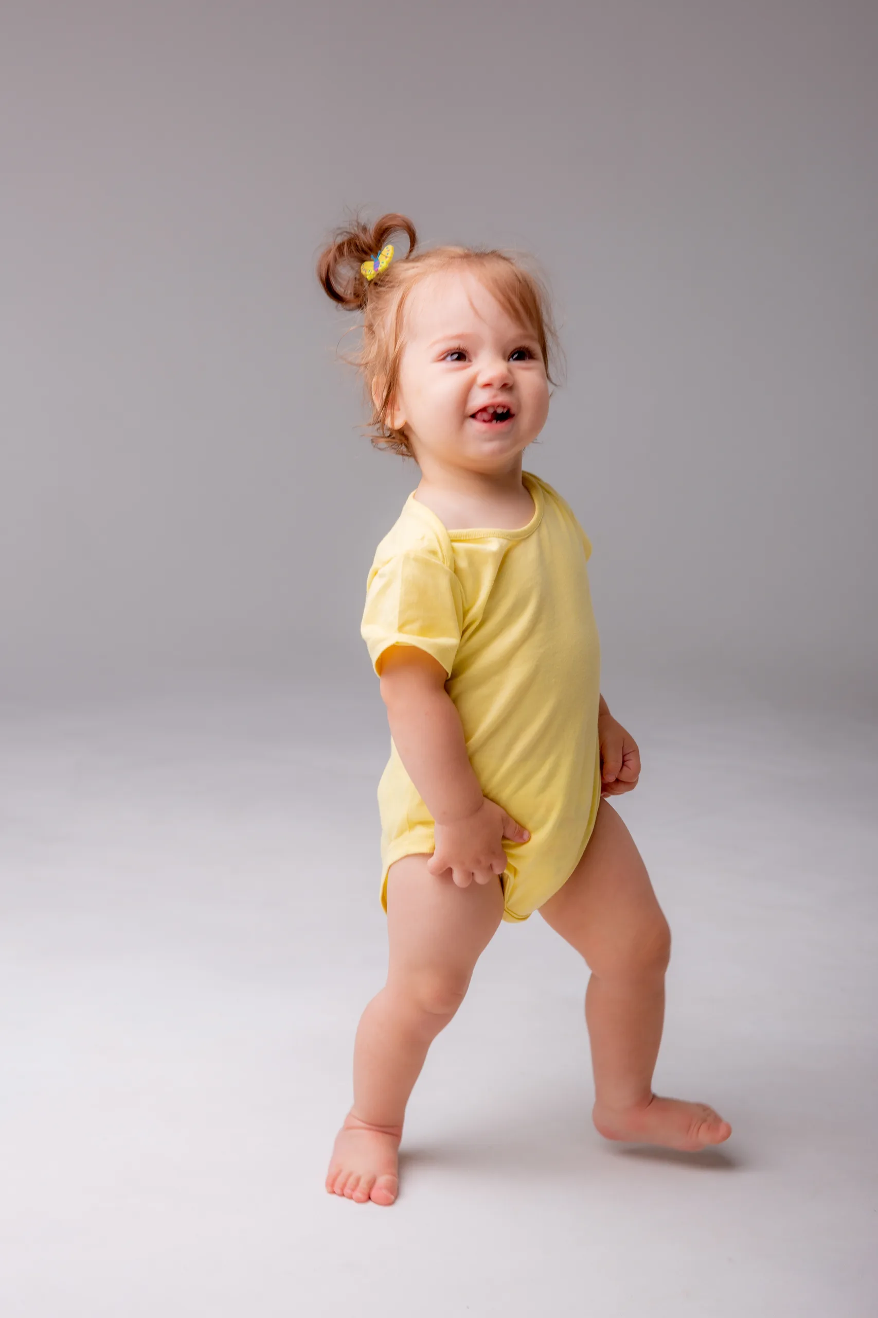 Toddler in a yellow romper standing in a studio