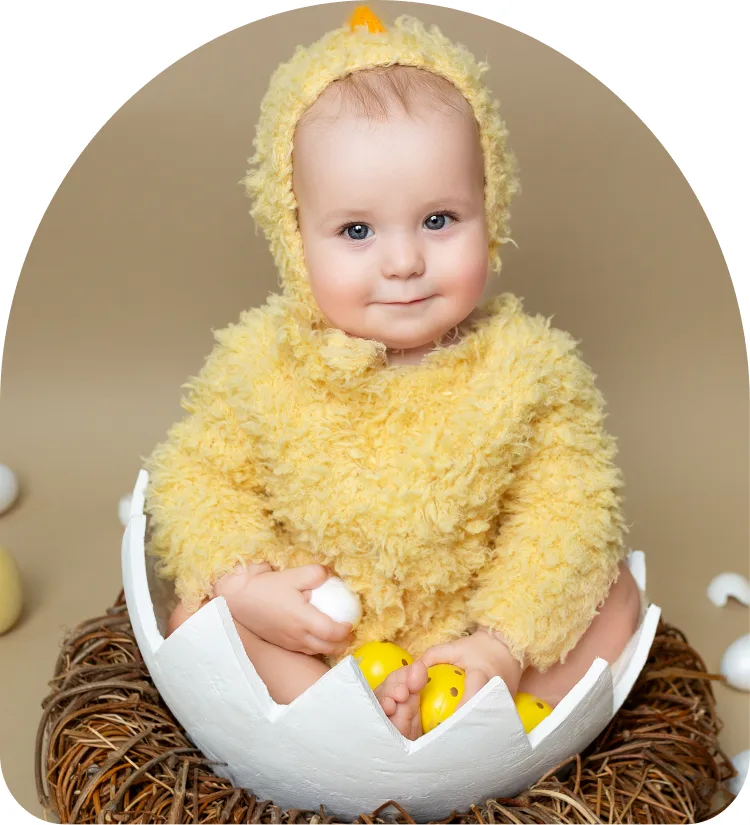 Baby in a yellow chick costume sitting in an eggshell