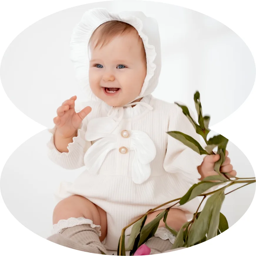 Baby in a white outfit holding a eucalyptus sprig