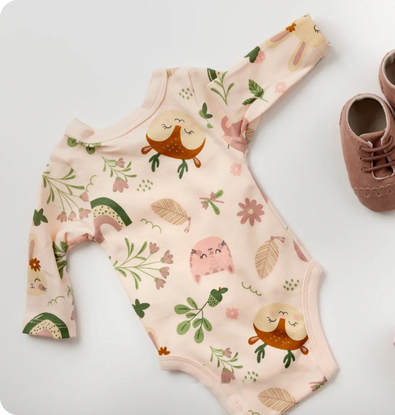 Flat lay of a pale pink printed romper beside a pair of tan baby shoes