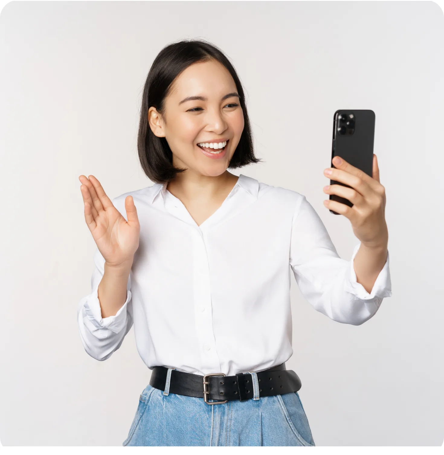 Smiling woman in a white shirt holding a phone up in front of a warm gray studio wall