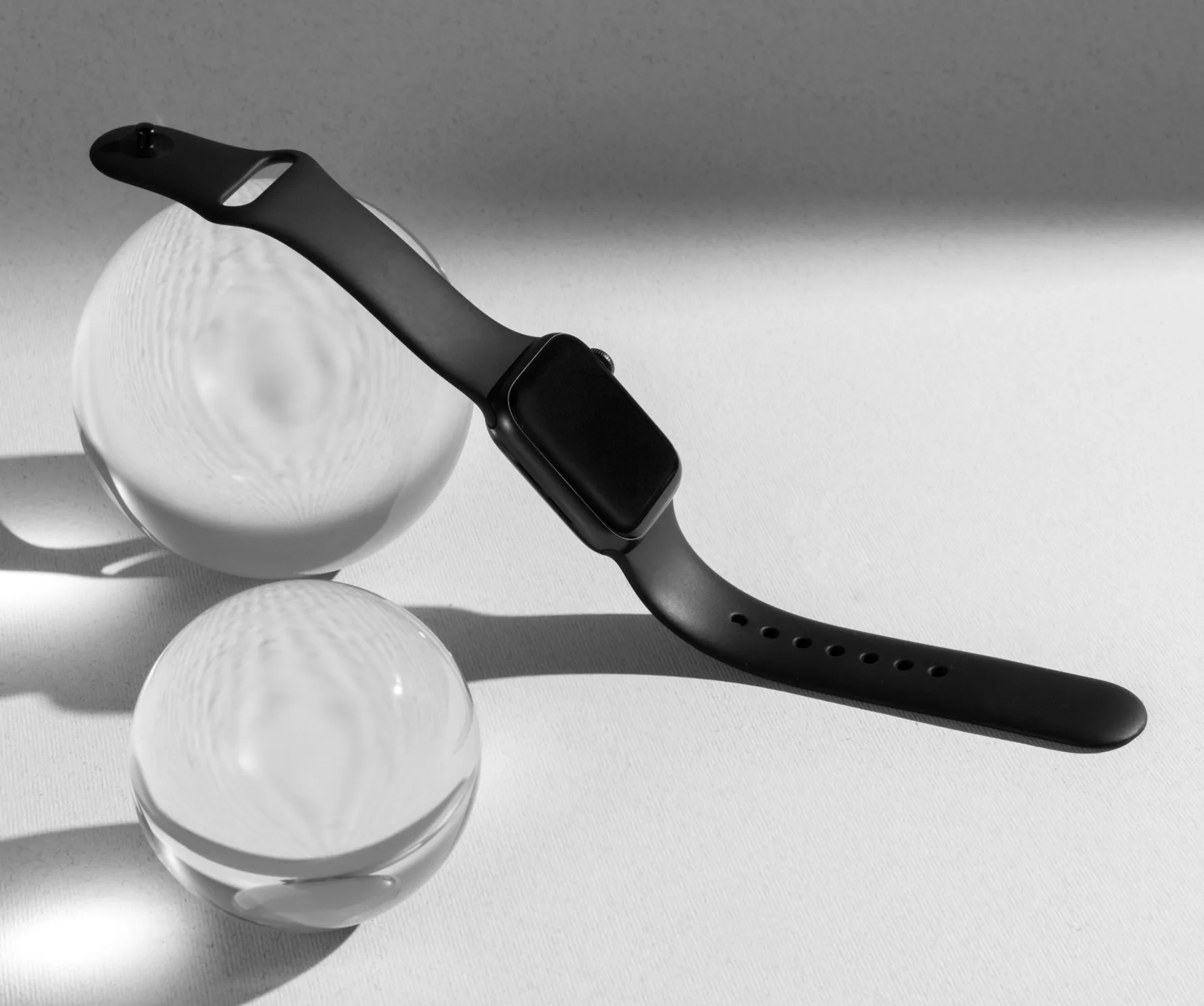 Black smartwatch resting on clear glass spheres in soft studio light