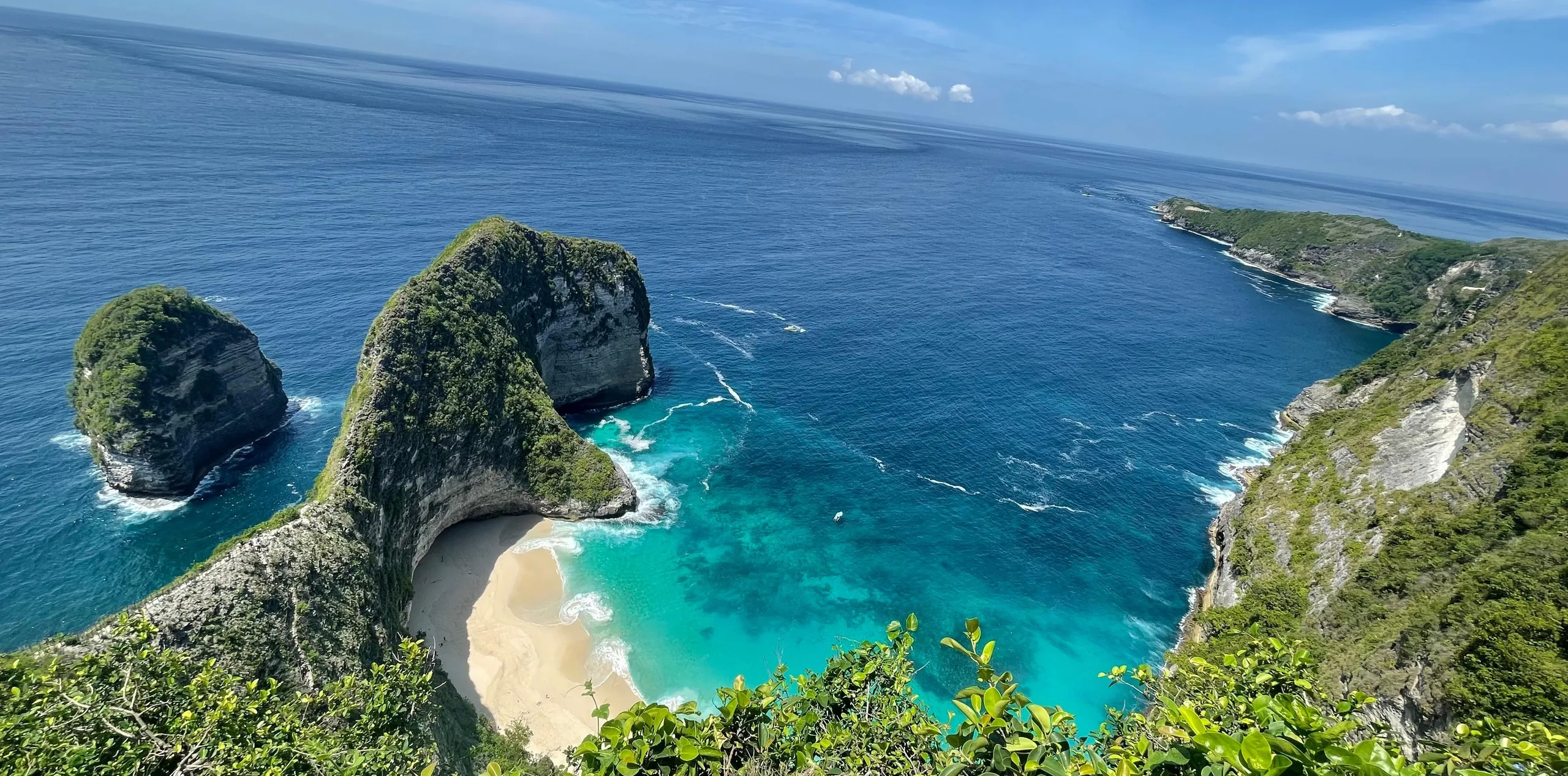 Aerial view of turquoise water and a curved green cliff above a hidden beach