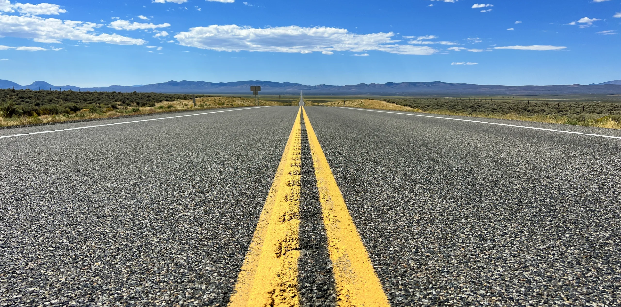Empty two-lane highway running to distant mountains under a wide blue sky