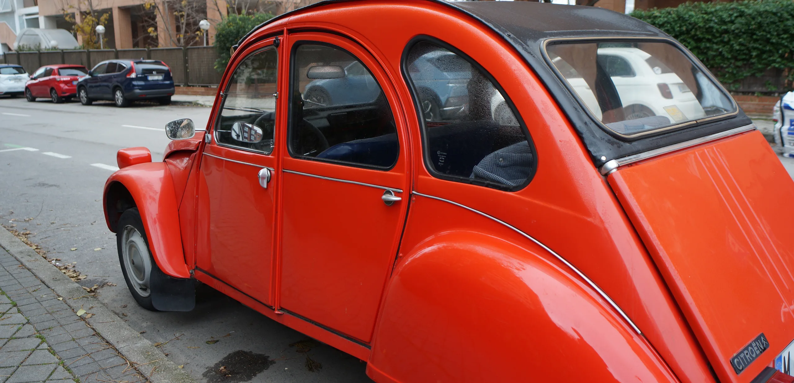 A bright orange vintage two-door car parked on a quiet street