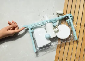 Hand reaching for a clear travel toiletry pouch of white bottles